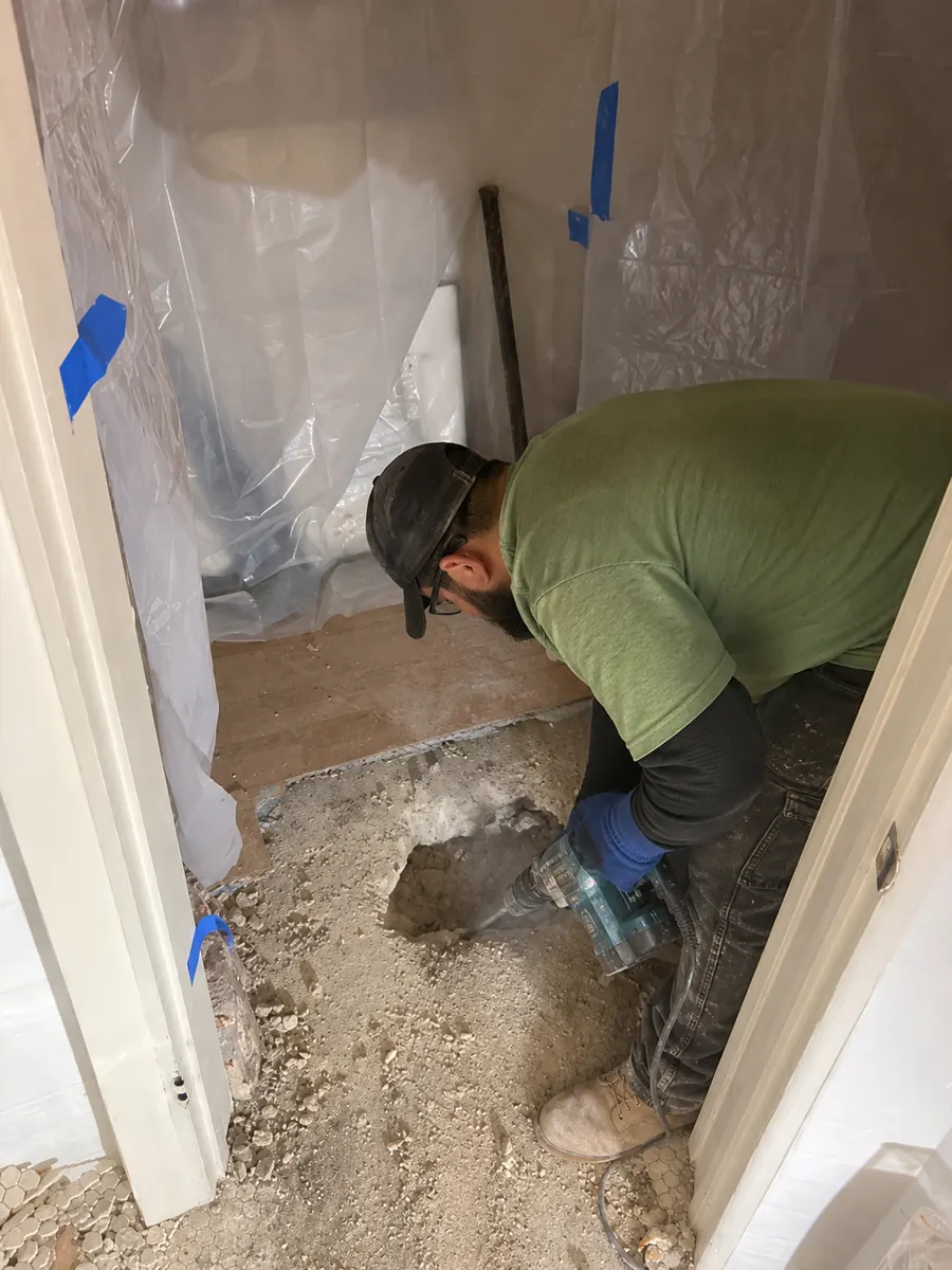 Precision Slab Opening After Leak Detection — Drain Master NJ Drain Master NJ technician opening one small precisely located section of slab to reach a leaking line, with the room fully protected