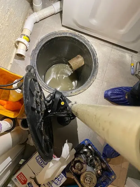 Sewage ejector pit opened with pump lifted for service beside a laundry area at a New Jersey home